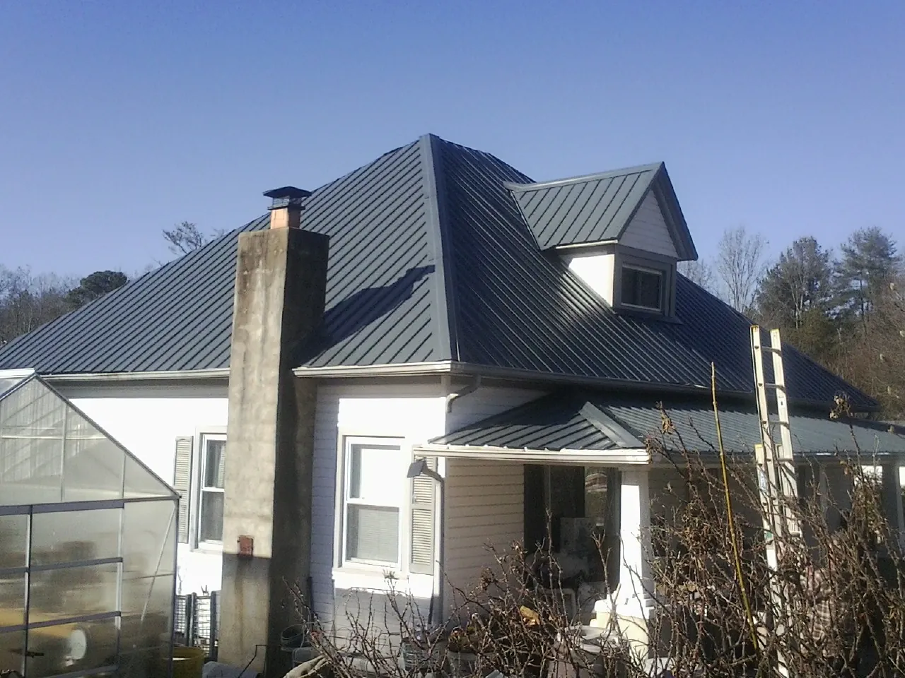 Dark blue standing seam metal roof on a white farmhouse with dormer — Slate & Tile Roof Repair by Roofing Brothers in Lostine