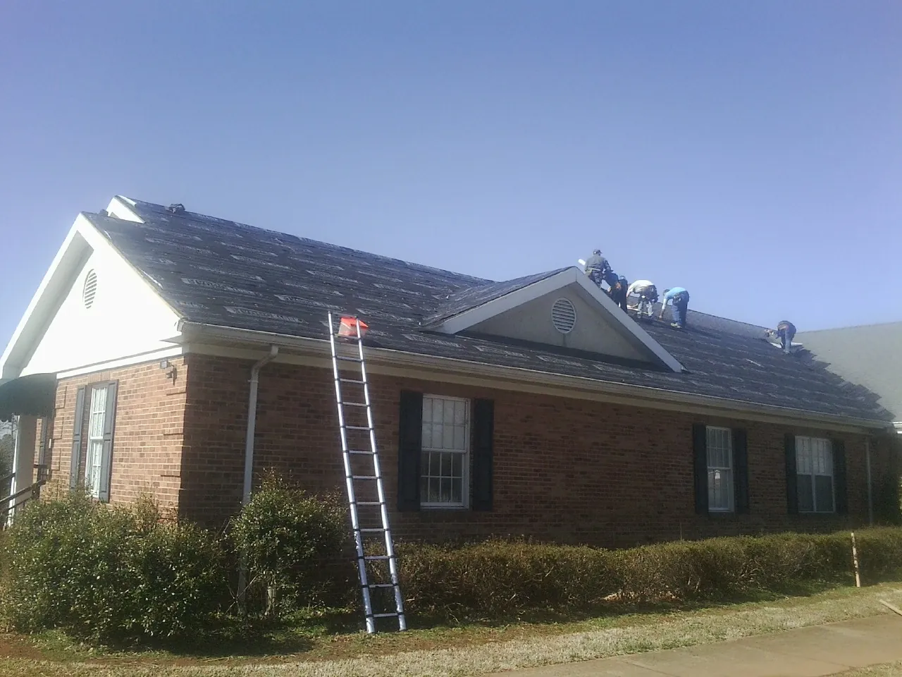 Crew tearing shingles off a brick ranch roof with a ladder set — Emergency Roof Repair work by our crew in Lostine