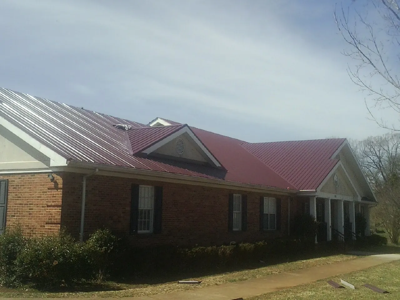 Red metal roof with gabled entries on a long brick building, from a Hail Damage Roof Repair job in Lostine