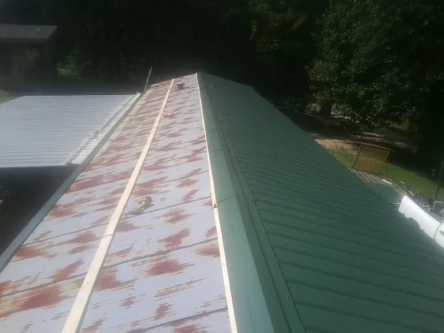 Old rusted panels beside newly installed green metal roofing — Wind Damage Roof Repair by Roofing Brothers in Lostine