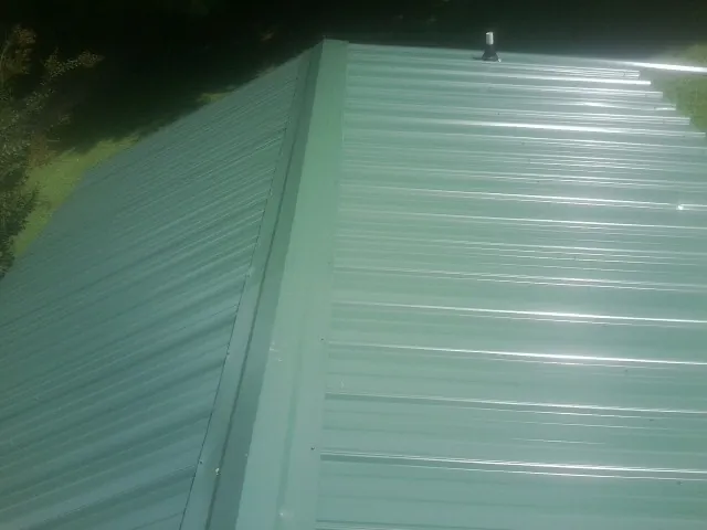 New green metal panels meeting at the ridge of a roof — Flat Roof Repair work by our crew in Lostine