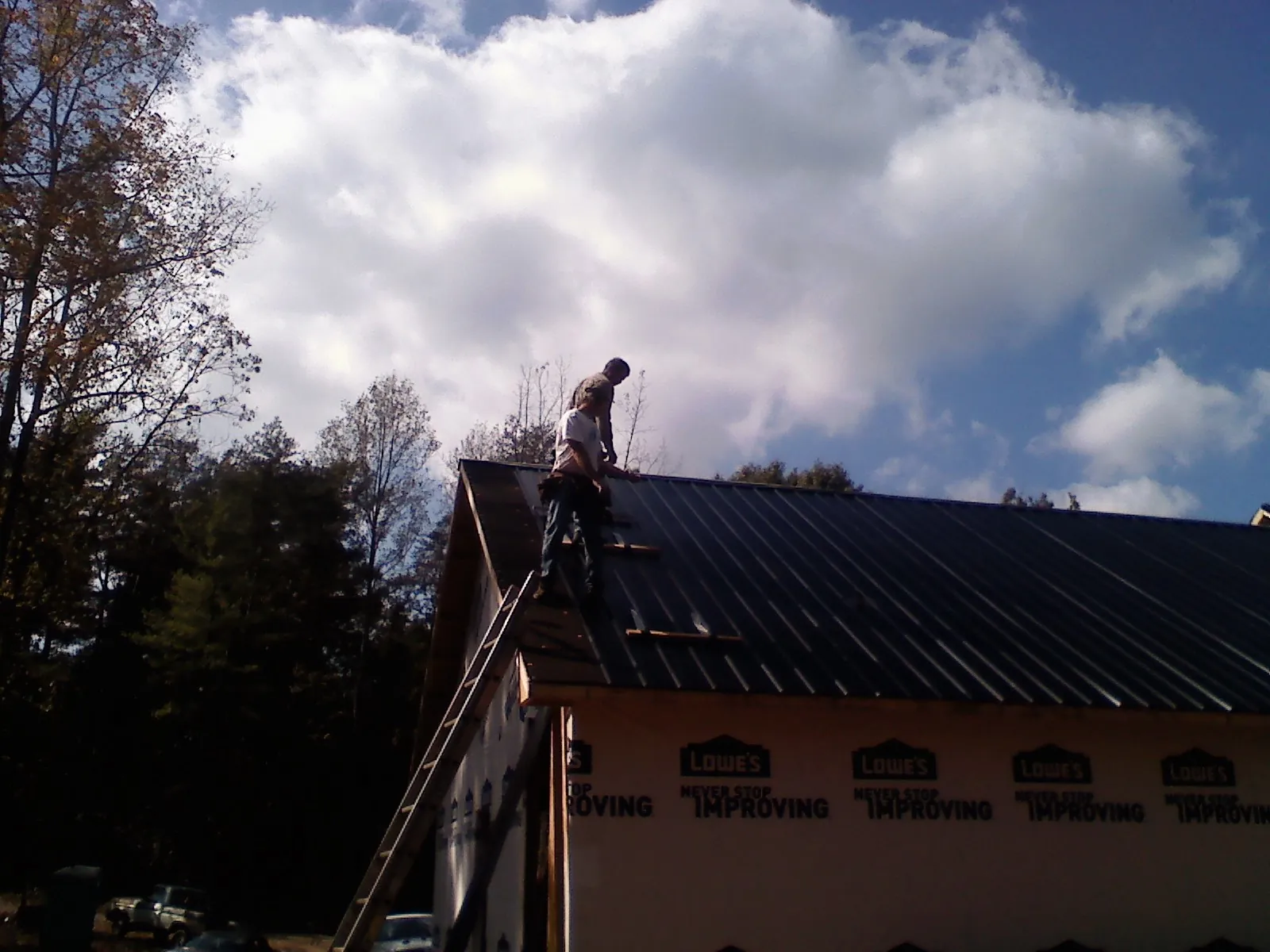 Roofer fastening dark metal panels high against a cloudy sky, from a Roof Inspection job in Lostine